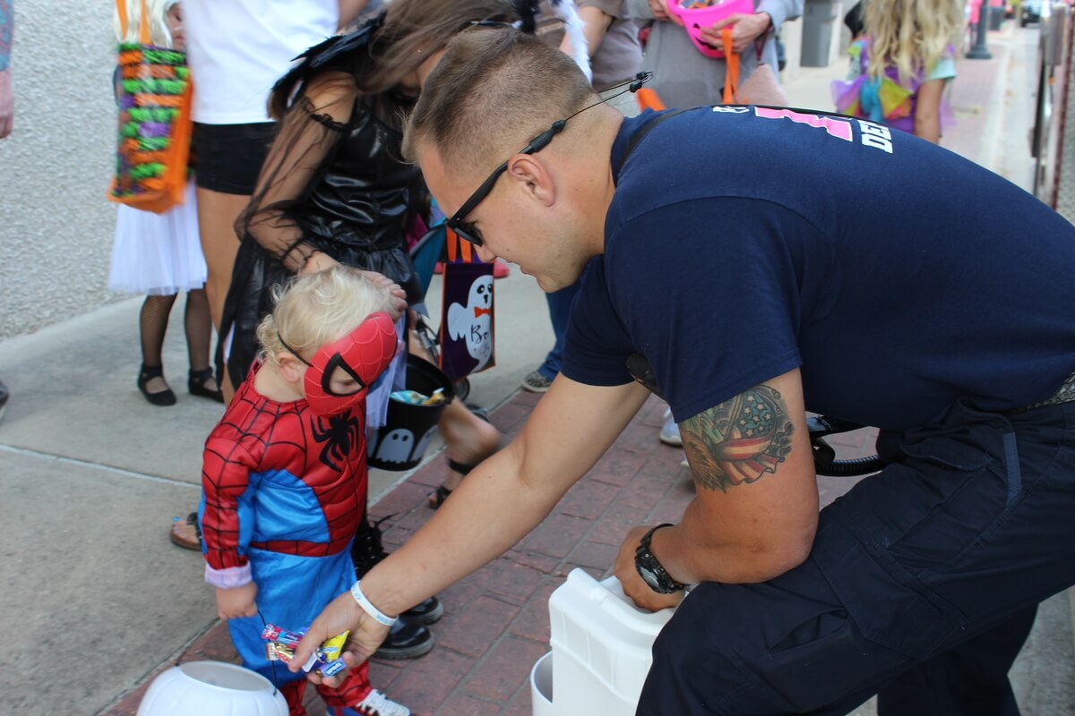Fire fighter handing candy to Trick or Treaters along Downtown