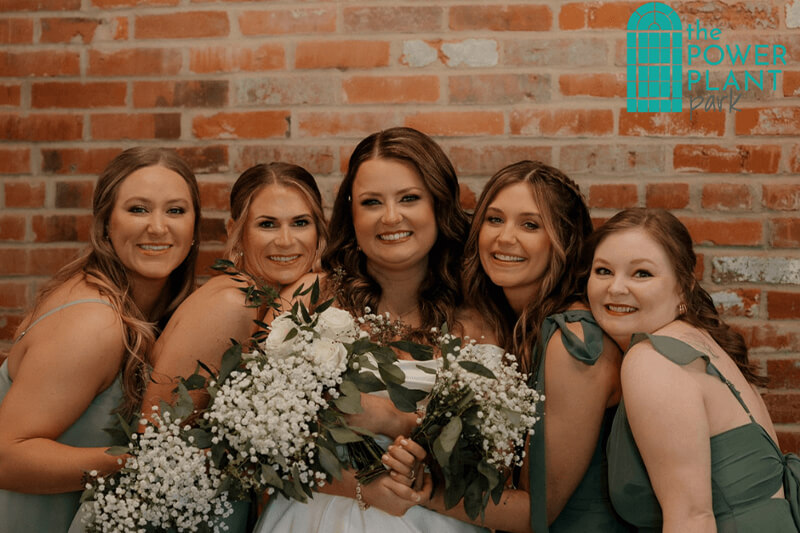 Bride and Bridesmaids smiling for a picture real close together and they are holding flowers.